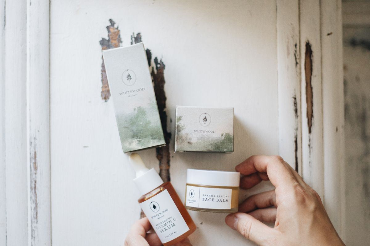 Hands holding skincare jars and a serum bottle