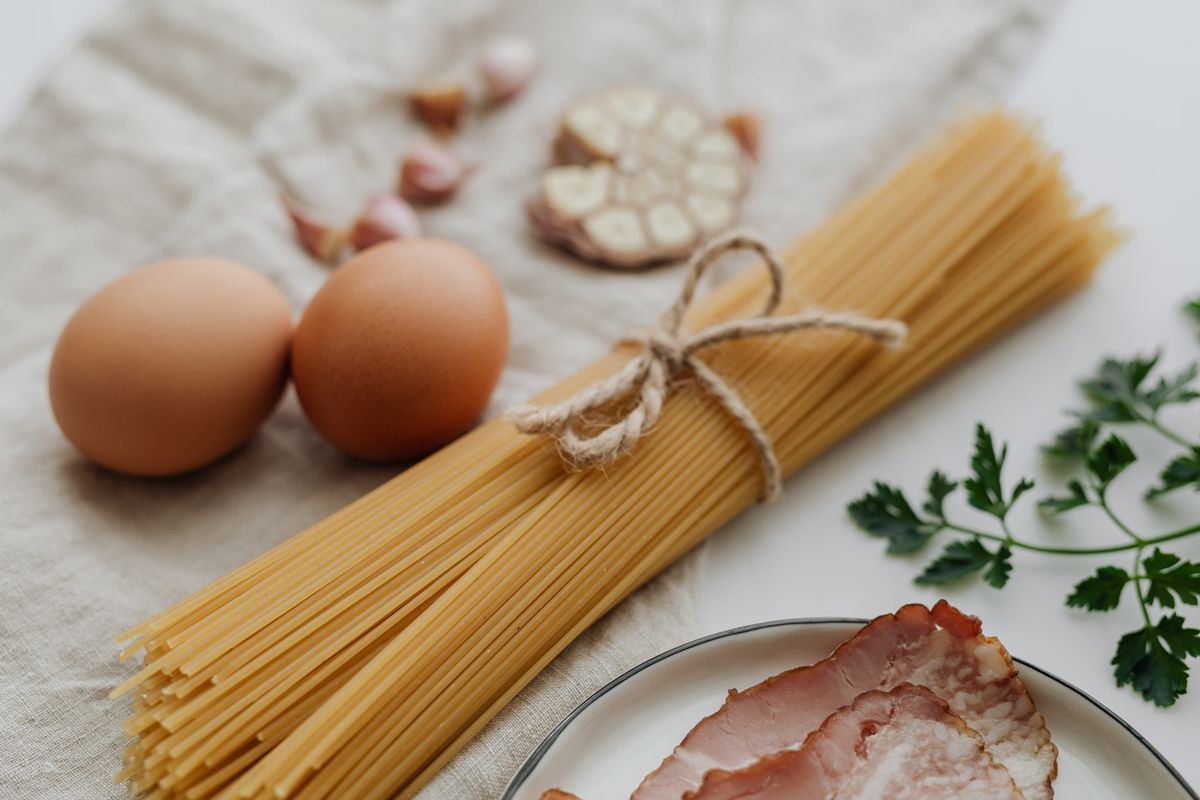 Spaghetti, eggs, garlic and herbs laid out on a table
